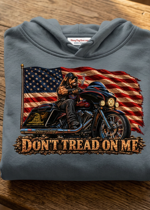 Front of the gray Don't Tread Doggo premium hoodie with the flag and motorcycle Don't Tread On Me graphic, laid flat on a wooden table