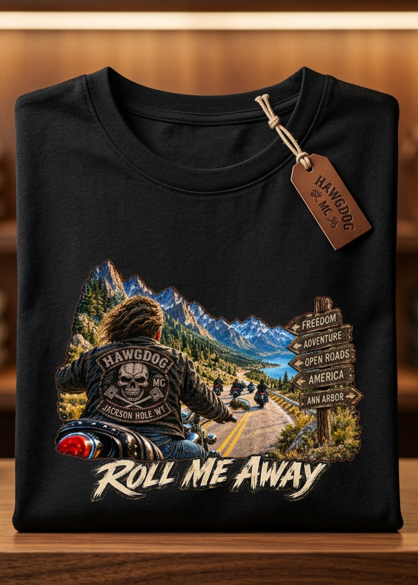 Front of the black Roll Me Away men's tank top with the mountain road motorcycle graphic, laid flat on a wooden table
