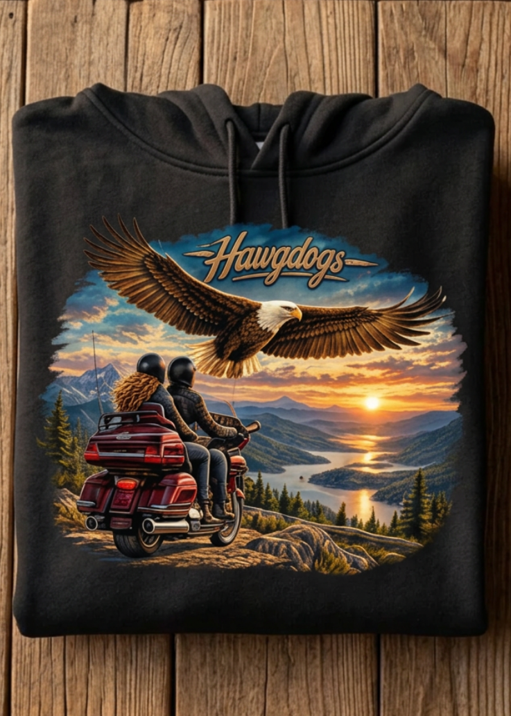 Front of the black Wings of The Open Road hoodie with the eagle and sunset motorcycle graphic, laid flat on a wooden table